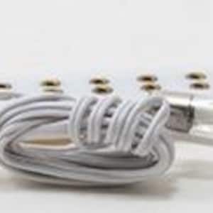 Puede incluir: Una tira de componentes eléctricos rectangular blanca con una serie de puntos de contacto metálicos, un fusible de vidrio sujeto por clips plateados y una pequeña bombilla. Un cable blanco está enrollado y unido a un segundo fusible de vidrio.