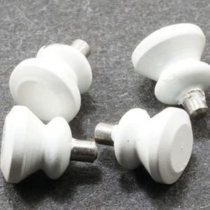 May include: Four white cabinet knobs with a smooth, rounded, hourglass-shaped profile. Each knob features a flat circular face and a metallic threaded screw post extending from the back, designed for attachment to furniture or cabinetry doors.