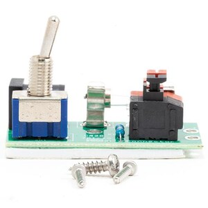 May include: A green printed circuit board featuring a silver metal toggle switch with a blue base, a small black push-button switch with a red top, and a tiny blue resistor. Two silver metal screws are positioned in front of the circuit board.