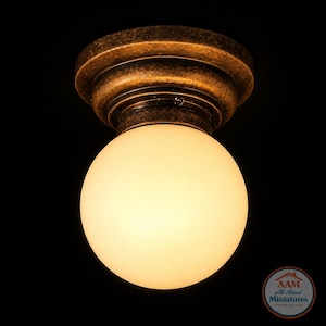 May include: A ceiling light fixture with a round, frosted glass globe. The fixture has a bronze-colored, ornate metal base. The light is illuminated, casting a warm glow against the black background. The fixture is a miniature.