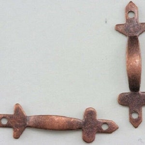 Könnte beinhalten: Zwei antike Kupfer-Schubladengriffe mit einem schlichten, eleganten Design. Jeder Griff hat einen abgerundeten, gebogenen Griff und ein dekoratives, kreuzförmiges Ende.