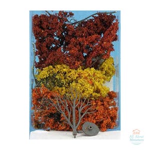 May include: A collection of miniature model trees in autumn colors including deep red, bright yellow, and burnt orange foliage. A single bare gray plastic tree frame with a circular base is positioned in the foreground of the clear plastic packaging.