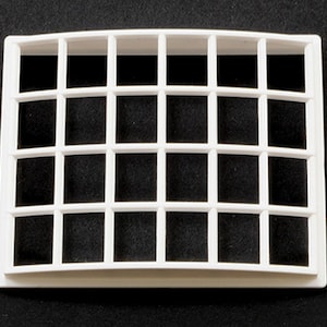 Op de afbeelding: Witte kunststof ventilatiekap met een gebogen bovenkant en een rasterpatroon van 24 vierkanten.