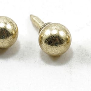 May include: Three gold-toned metal upholstery tacks, each featuring a smooth, spherical head attached to a straight, pointed nail shank. The metallic surface has a reflective finish with subtle variations in texture across the round heads.