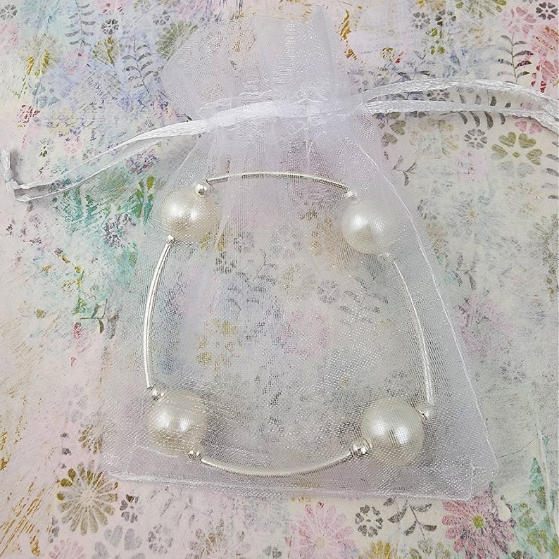 May include: A silver bangle bracelet with four white pearl beads. The bracelet is in a white organza bag.
