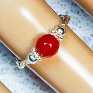 May include: A silver ring with a red gemstone. The ring is made of small silver beads that are twisted together.