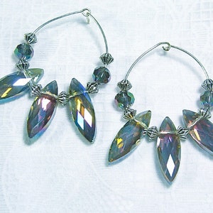 May include: A pair of hoop earrings with iridescent, teardrop-shaped crystals. The earrings feature a silver-tone metal wire and are adorned with faceted beads. The crystals reflect shades of blue, purple, and yellow.