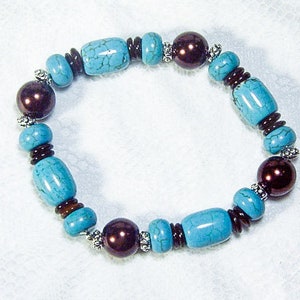 May include: A turquoise and brown beaded bracelet. The bracelet features a mix of turquoise-colored, oval-shaped beads and dark brown, round beads. Small silver-colored beads separate the larger beads. The bracelet is on a white background.