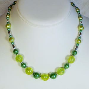 May include: A beaded necklace with a mix of green and yellow beads. The necklace features a variety of bead sizes and textures, including round, crackled, and smooth beads. The beads are strung together with silver-colored metal accents.