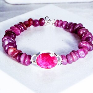May include: A pink gemstone bracelet with a large oval-shaped pink gemstone in the center. The bracelet is made of small, round pink gemstones.