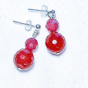 May include: A pair of silver earrings with two red gemstone beads on each earring.