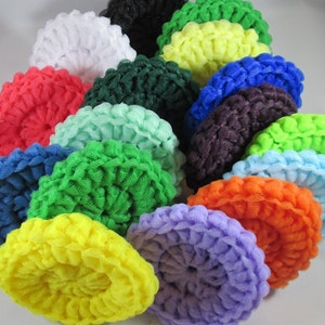 May include: A collection of colorful, round, crocheted scrubbies in various shades, including red, blue, green, yellow, and purple. The scrubbies have a textured surface and are arranged in a circular pattern.