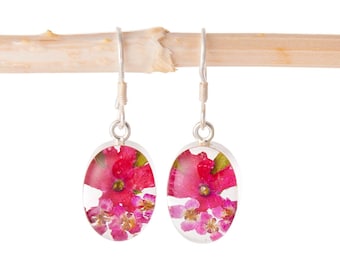 May include: A pair of silver earrings with oval-shaped pink flower accents encased in clear resin.