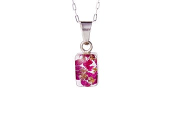 May include: A silver necklace with a rectangular pendant. The pendant is filled with pink and gold dried flowers encased in clear resin. The chain is delicate and the pendant hangs from a small loop.