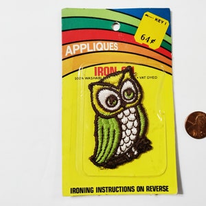 May include: Iron-on applique featuring a green and brown owl with white accents. The applique is packaged on a yellow card with the text "Appliques", "Iron-On", "100% Washable", "Vat Dyed", and "Ironing Instructions on Reverse". The card also has a price tag that says "Key I 64¢".