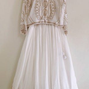 May include: A white, floor-length skirt with gold embroidery and a matching white crop top with gold and pearl embellishments.
