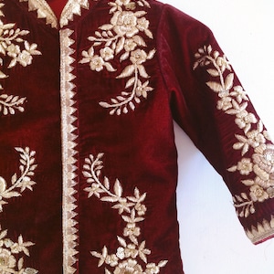 May include: A maroon velvet jacket with gold embroidery of floral designs. The jacket has a mandarin collar and long sleeves.