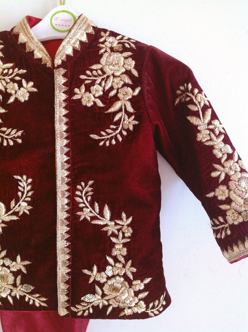 May include: A maroon velvet jacket with gold embroidery of floral designs. The jacket has a mandarin collar and long sleeves.