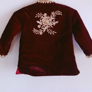 May include: A maroon velvet jacket with gold embroidery of a floral design on the back.