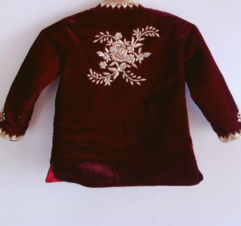 May include: A maroon velvet jacket with gold embroidery of a floral design on the back.