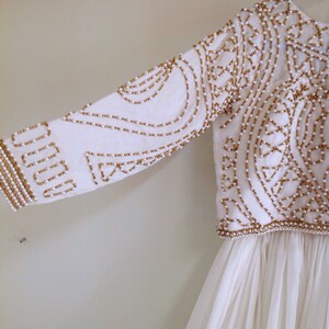 May include: White dress with a gold and white beaded bodice. The bodice has a geometric pattern and the skirt is flowing.
