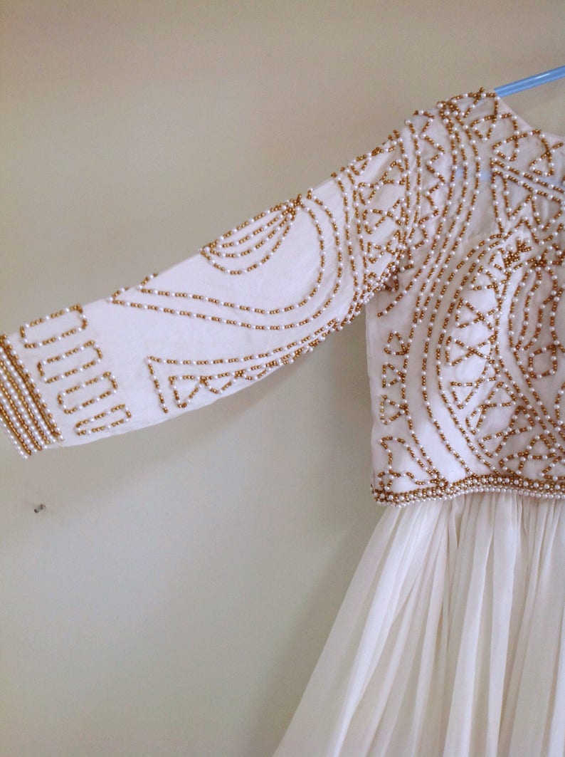 May include: White dress with a gold and white beaded bodice. The bodice has a geometric pattern and the skirt is flowing.