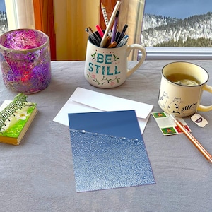 May include: A white ceramic mug with a black handle and the text "But First, Coffee" in a bold, black font. The mug is set against a neutral background, highlighting its simple design.