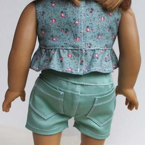 Peut inclure: Une poup&eacute;e portant un haut sans manches &agrave; imprim&eacute; floral vert avec un ourlet &agrave; volants et un short en jean vert. La poup&eacute;e porte des baskets ray&eacute;es arc-en-ciel avec le mot "Maddies" dessus.