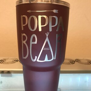 May include: A maroon Yeti tumbler with a silver design that says "Poppa Bear" with an arrow and a teepee graphic.