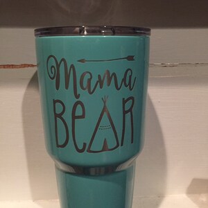 May include: A turquoise Yeti tumbler with a silver vinyl decal that reads "Mama Bear" with a small arrow and a teepee design.