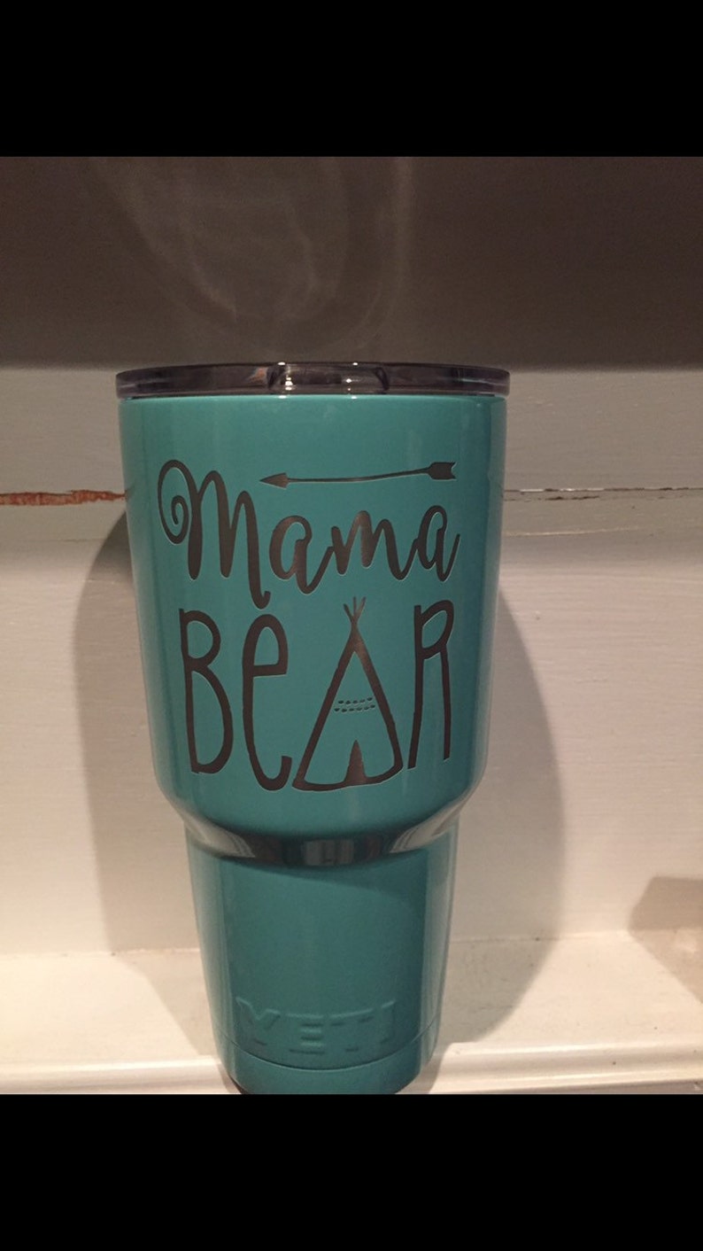 May include: A turquoise Yeti tumbler with a silver vinyl decal that reads "Mama Bear" with a small arrow and a teepee design.