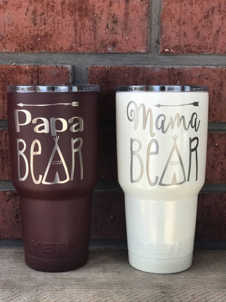 May include: Two stainless steel tumblers with lids. The tumbler on the left is brown with the text "Papa Bear" and a teepee design. The tumbler on the right is white with the text "Mama Bear" and a teepee design.