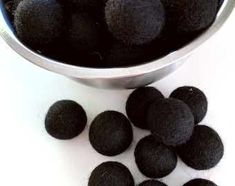 May include: A bowl filled with black felt balls. There are also black felt balls scattered on a white surface.