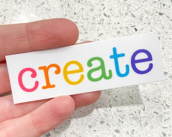 Puede incluir: Una pegatina blanca con la palabra "create" escrita en colores arcoíris. Las letras están delineadas en negro y tienen una fuente redondeada.