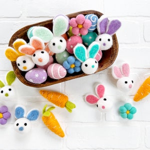 May include: A wooden bowl filled with felt Easter decorations, including bunnies, eggs, flowers, and carrots. The decorations are in various colors, including pink, blue, green, yellow, and purple.