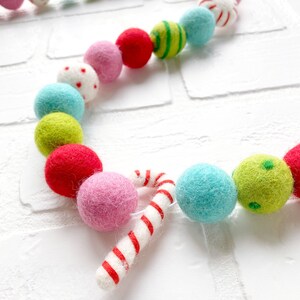 Pode incluir: Uma guirlanda colorida de bolas de feltro com um design festivo. A guirlanda apresenta uma variedade de bolas de feltro redondas em tons de rosa, vermelho, verde e azul, juntamente com detalhes de bengalas doces. As bolas t&ecirc;m desenhos listrados, de bolinhas e s&oacute;lidos.