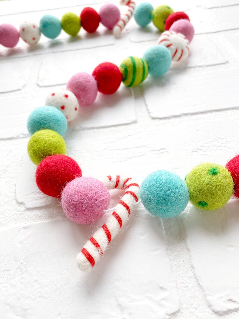 Pode incluir: Uma guirlanda colorida de bolas de feltro com um design festivo. A guirlanda apresenta uma variedade de bolas de feltro redondas em tons de rosa, vermelho, verde e azul, juntamente com detalhes de bengalas doces. As bolas t&ecirc;m desenhos listrados, de bolinhas e s&oacute;lidos.