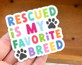 May include: A colorful sticker with the text "RESCUED is MY FAVORITE BREED" and two paw prints. The text is in a rainbow of colors, with each letter in a different color.