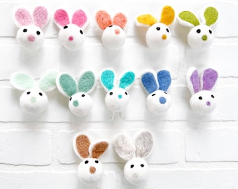 May include: Twelve felt bunny ornaments in various colors, including pink, green, blue, yellow, orange, and purple. The bunnies have white faces with black eyes and noses.
