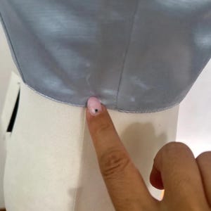 Puede incluir: Primer plano del borde inferior de una tela de sat&eacute;n azul claro. La tela es lisa y tiene un ligero brillo. La tela est&aacute; siendo sostenida por una mano.