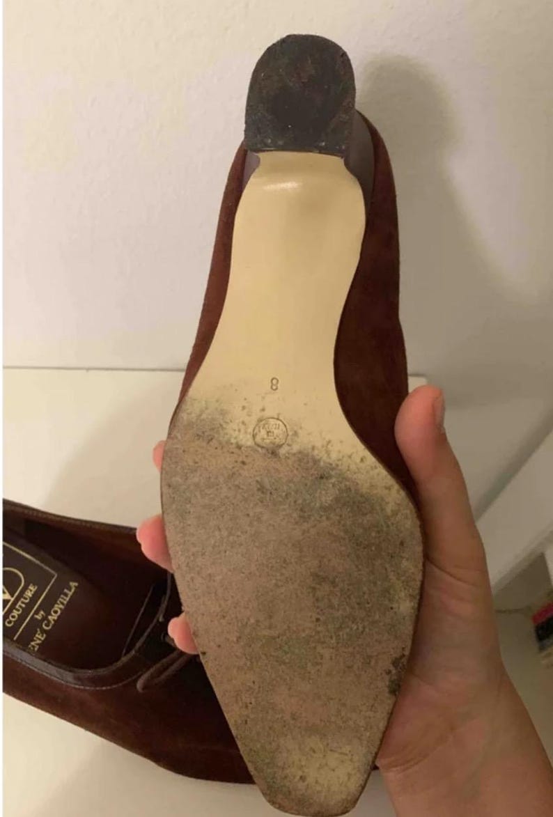 May include: Brown suede high-heeled shoe with a pointed toe. The sole is a light beige color, and the heel is dark brown. The shoe size is 8. The shoe is labeled "COUTURE by Rene Caovilla".