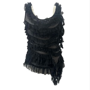 May include: Black sleeveless top with multiple layers of ruffled fabric. The top has a flowing, asymmetrical design with a cascade of ruffles on one side. The garment is made of a sheer material.