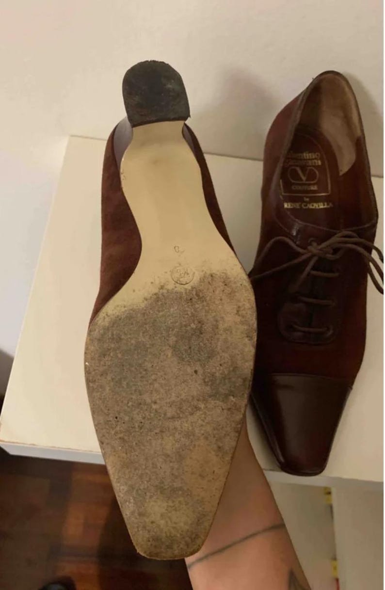 May include: Pair of vintage burgundy suede and leather heeled shoes. The shoes have a pointed toe and lace-up design. The soles show wear. The heel height is approximately 2 inches.
