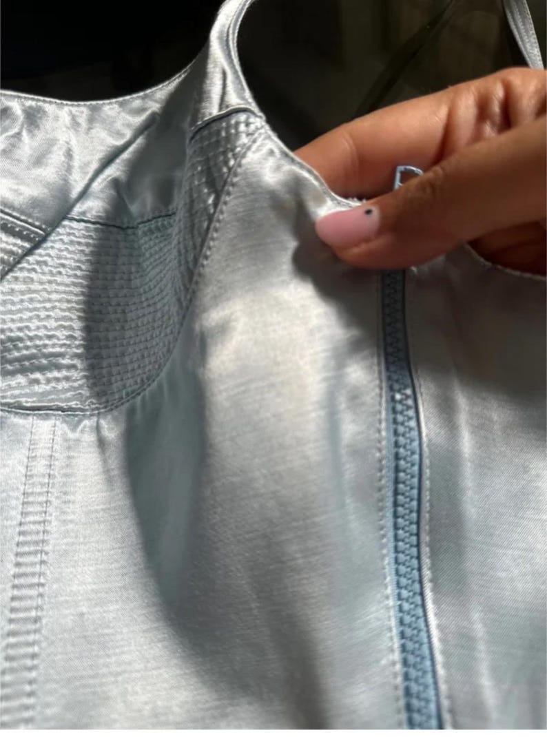 Puede incluir: Una blusa de sat&eacute;n azul claro con cierre de cremallera y un detalle de puntada decorativa.