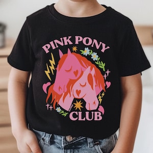 May include: Black t-shirt with a pink and red graphic of two cartoon ponies with the text "Pink Pony Club" in pink and yellow letters.