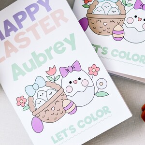Puede incluir: Un libro para colorear blanco con un t&iacute;tulo "Feliz Pascua" en rosa, morado y verde. El libro presenta una linda ilustraci&oacute;n de una cesta de huevos y un solo huevo con un lazo. El libro est&aacute; personalizado con el nombre "Aubrey" y dice "Vamos a colorear".