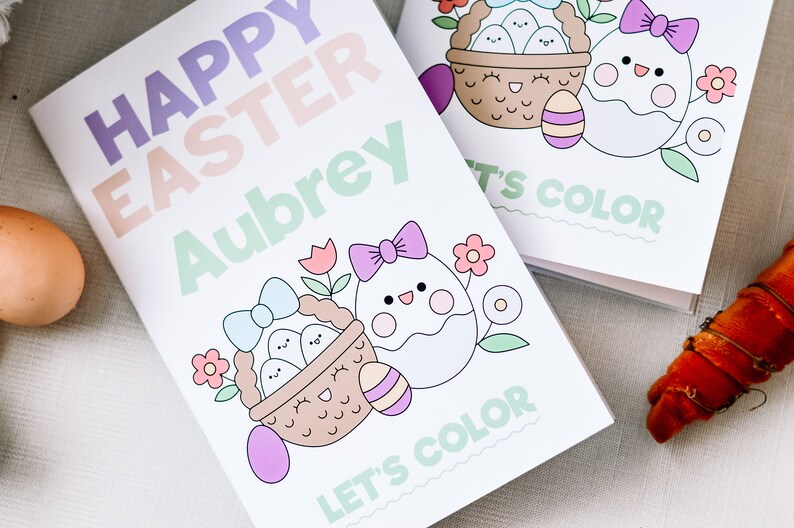 Puede incluir: Un libro para colorear blanco con un t&iacute;tulo "Feliz Pascua" en rosa, morado y verde. El libro presenta una linda ilustraci&oacute;n de una cesta de huevos y un solo huevo con un lazo. El libro est&aacute; personalizado con el nombre "Aubrey" y dice "Vamos a colorear".