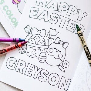 Puede incluir: Una p&aacute;gina para colorear con el texto "Happy Easter" y el nombre "Greyson" en la parte inferior. La p&aacute;gina presenta una cesta de huevos de Pascua con una flor y un solo huevo con un lazo. Se muestran crayones Crayola junto a la p&aacute;gina.