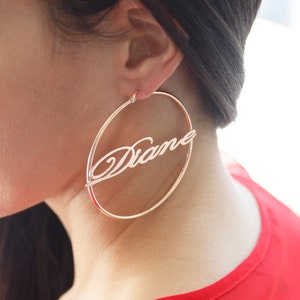 May include: Gold hoop earrings with the name "Diane" written in cursive across the front.