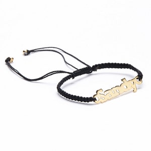 May include: A black string bracelet with a gold nameplate charm that says "Samoyed".